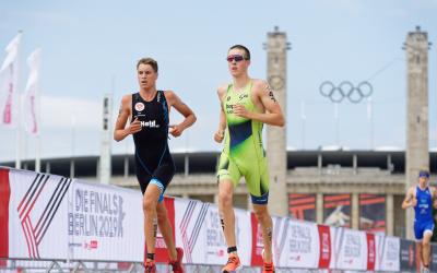 Zwei Triathleten laufen gemeinsam im Hintergrund sind die Olympischen Ringe zu sehen